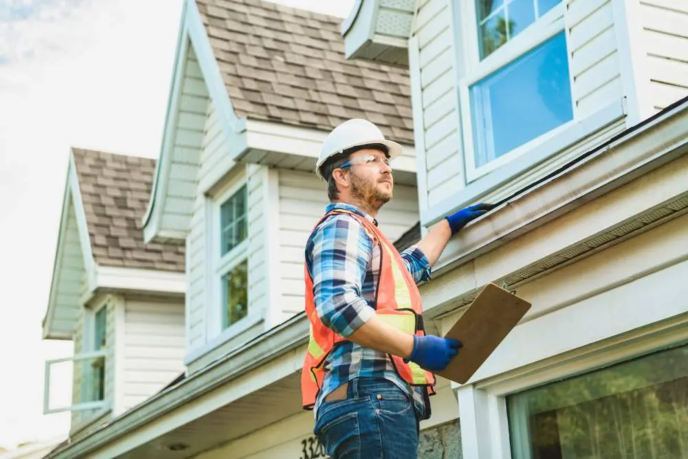 Man With Hard Hat Standing On Steps Inspecting House Roof