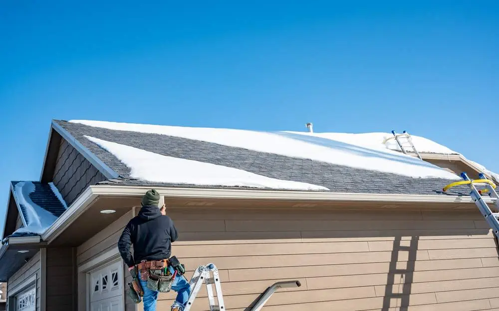 Contractor Installing Gutters On A Residential Building In The Winter With Snow On The Roof