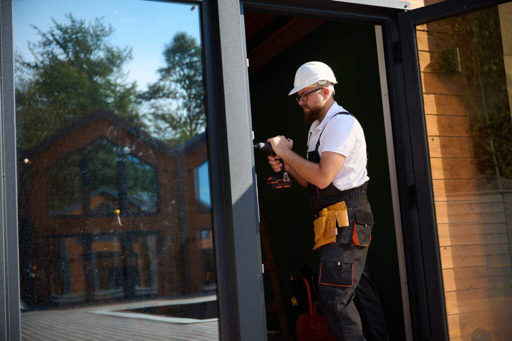 Construction Worker Installing Door In A New House Construction Site Man In Working Attire Install Front Door Builder In Uniform With Screwdriver Adjusting Front Glass Door In New Beautiful House