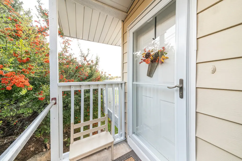 Entrance Of A House With Glass Storm Door Over The White Door With Hanging Flower Decoration