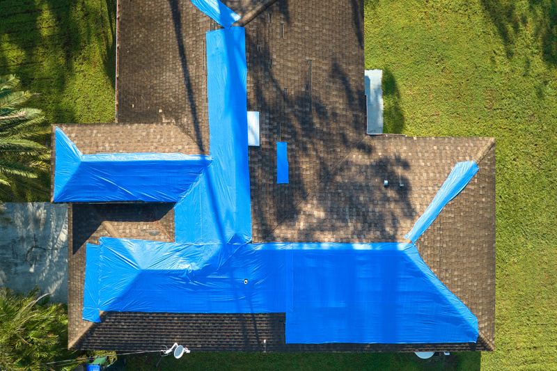 Top View Of Leaking House Roof Covered With Protective Tarp Sheets Against Rain Water Leaks Until Replacement Of Asphalt Shingles Damage Of Building Rooftop As Aftermath Of Hurricane Ian In Florida
