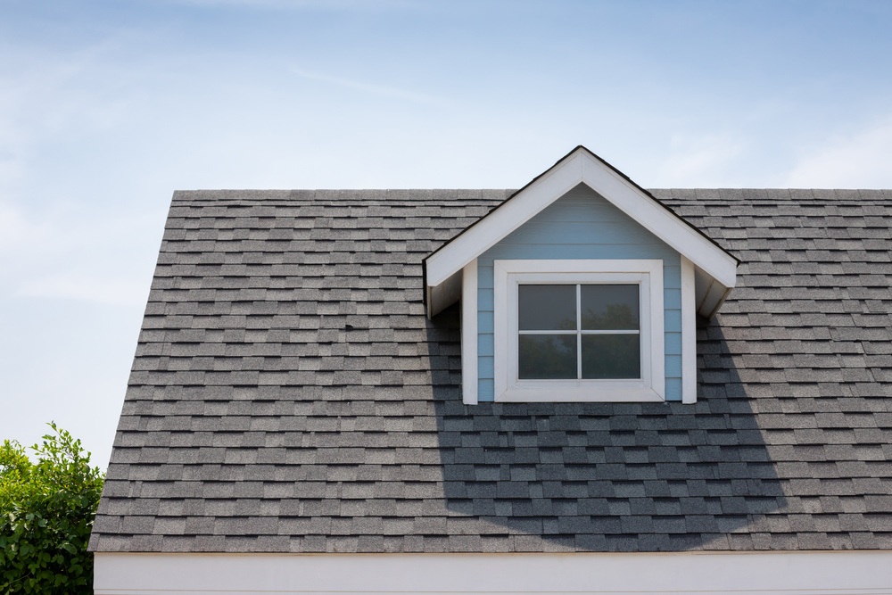Roof shingles with garret house on top of the house among a lot of trees. dark asphalt tiles on the roof background