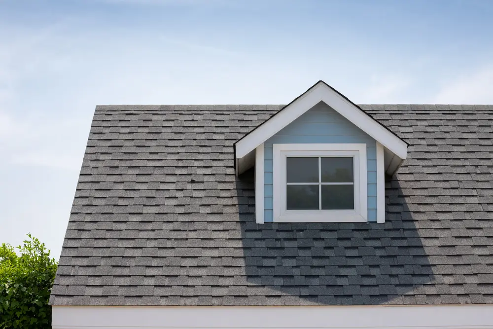Roof shingles with garret house on top of the house among a lot of trees. dark asphalt tiles on the roof background